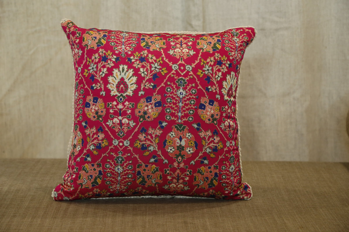 Ruby red floral silk cushion cover, angled view on a woven bench